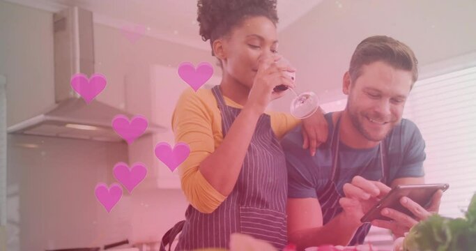 Animation of hearts over diverse couple cooking together and using tablet in kitchen at home