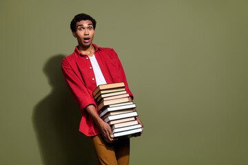 Photo of impressed funny man dressed red shirt carrying huge book pile empty space isolated green color background