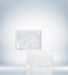 Crystal clear ice blocks in a rectangle form, stacked on a mirror surface on a white background.