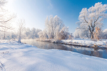 Majestic winter scenery with foggy river with crispy rime on a trees on a snowy riverbanks.