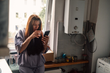 Multitasking at ease, a woman sips her morning tea while scrolling through her phone