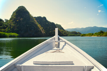 Prow of a white boat heading towards the lush greenery and limestone cliffs of Langkawi UNESCO-listed Geopark in Malaysia