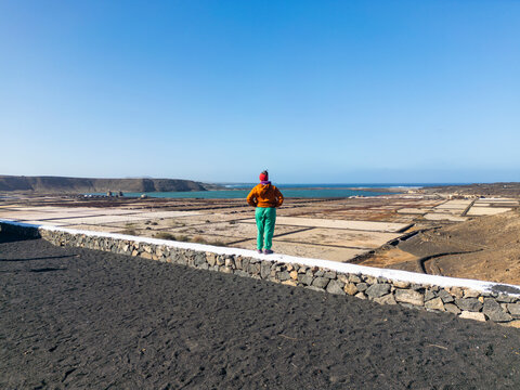 Back view of persone stands in contemplation, gazing over the vast and intricate salt flats stretching towards the sea in Lanzarote
