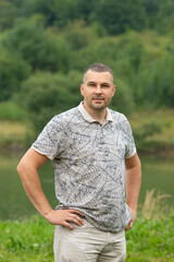 Vertical photo of handsome man in nature on the background of the lake. Summer concept.