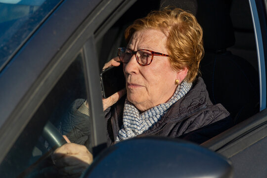 Elderly woman committing a traffic violation, talking on the phone driving a car.