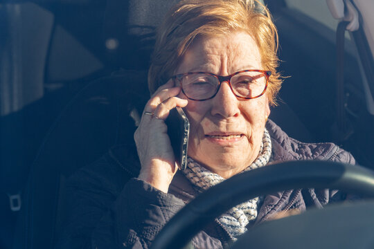 Elderly woman committing a traffic violation, talking on the phone driving a car.