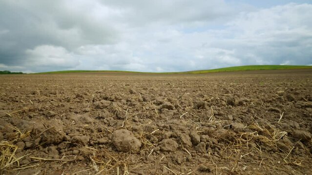Ploughed Agricultural Field Under Cloudy Sky. Brown soil of a plowed field with remnants of straw, against a cloudy sky.