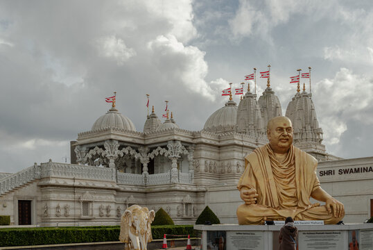 London, UK - Feb 23, 2024 - Exterior view of the Neasden temple (BAPS Shri Swaminarayan Mandir) and The gold colored statue depicts the late spiritual leader Pramukh Swami Maharaj against a nice cloud