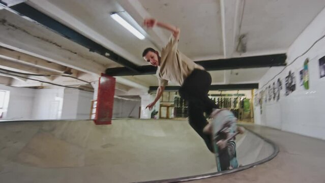 Young professional skateboarder skating bowl and performing fly out trick while training at skatepark