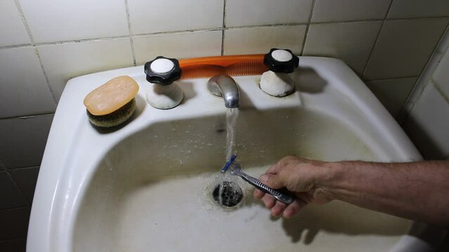 El hombre lava su navaja despu&eacute;s de afeitarse en un viejo ba&ntilde;o blanco, bajo agua corriente para limpiar la espuma de afeitar para el cuidado personal rutinario de su vida diaria