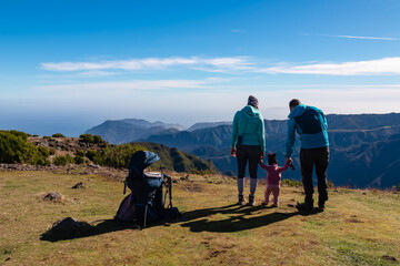 Hiker parents with small child walking on meadow overlooking coastline of Atlantic Ocean on Madeira...