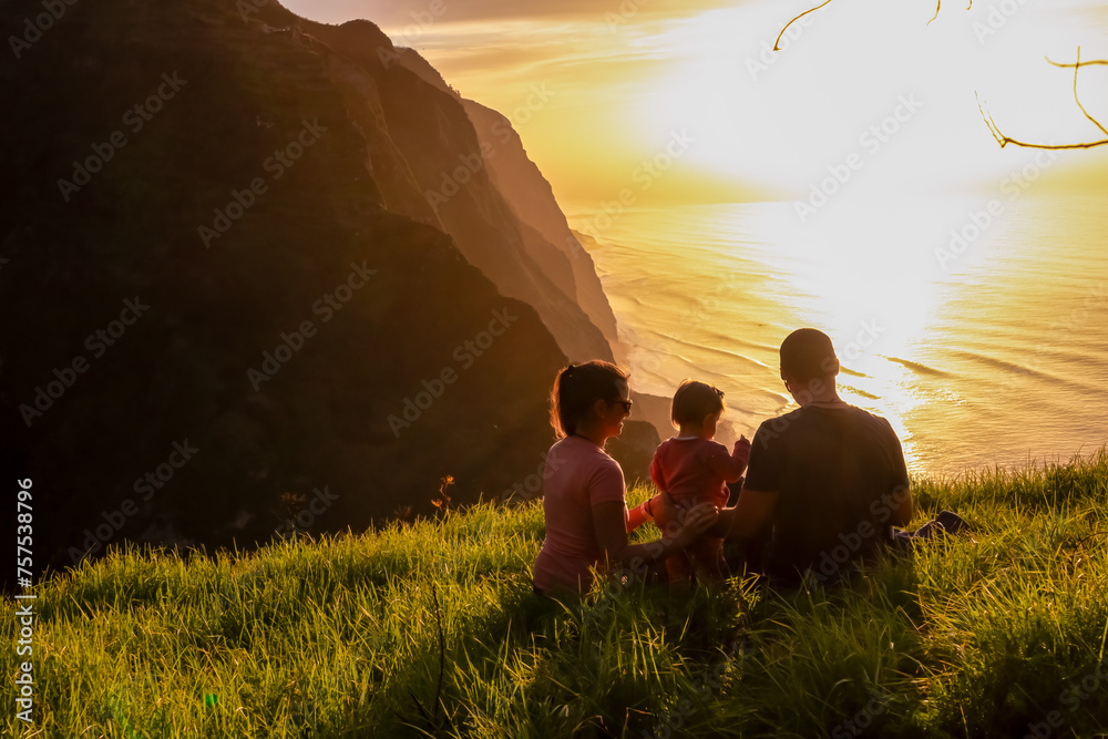 Wall mural family with child on meadow watching breathtaking sunset at viewing point miradouro do ponta da lade - Wall murals