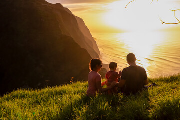 Family with child on meadow watching breathtaking sunset at viewing point Miradouro do Ponta da Ladeira, Madeira island, Portugal, Europe. Panoramic view of majestic coastline of Atlantic Ocean. Awe