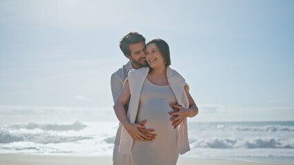 Expectant parents standing ocean beach at sunlight. Couple enjoying pregnancy