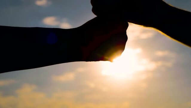 Close up: silhouettes of man and woman hands are bumping fists against the sunset or sunrise sky - sun lens flares. Informal greeting, giving dap, agreement, friendship and teamwork concept