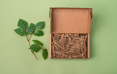 Mockup. Open cardboard box with paper filling on green background with green leaves top view.