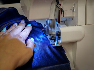 Female hand sewing on overlock machine, manufacture of clothes. Close up of sewing process in the factory.
