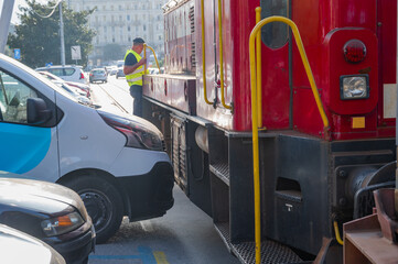 A freight train carrying shipping containers has difficulty moving between parked cars....