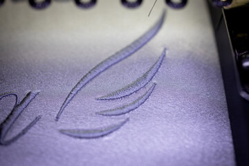 Embroidery wings with grey thread on a white satin robe for the bride.