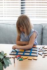 A cute girl is playing a logical wooden game at a table in a room. Children's wooden educational toy