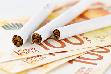 Cigarettes are on 100 shekel bills. Concept of big expenses, big price or taxes. - obrazy, fototapety, plakaty