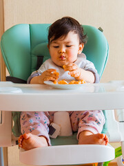 Bebe en su silla de comer usando sus manos para comer su fruta