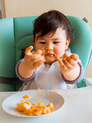 Bebe en su silla de comer usando sus manos para comer su fruta