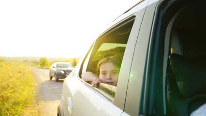 child girl face looks smiling from car out window, enjoying summer freedom during trip, trip, hand, summer time, catches wind with his hand from car window, children dream, car driving time, car