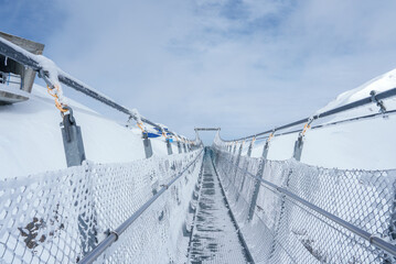 A serene, snowcovered pedestrian bridge at Engelberg ski resort, Switzerland, with metal cables,...