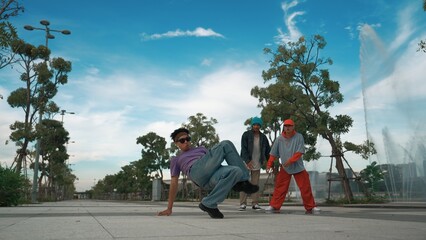 Asian skilled hipster doing freeze pose at camera surrounded by break dancer team near fountain...