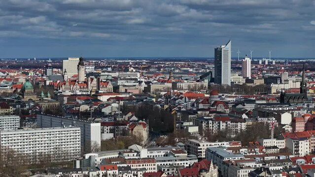 Slow flight towards downtown Leipzig. telephoto shot. The new town hall can be seen. Other landmarks are also in the picture. The old town, new buildings, wind turbines and an airplane in the sky.