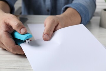 Man with papers using stapler at white wooden table, closeup