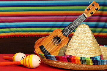 Mexican sombrero hat, ukulele and maracas on red table, closeup