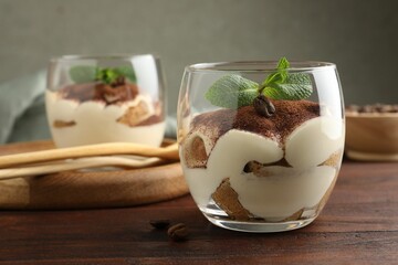 Delicious tiramisu in glasses, mint leaves and coffee beans on wooden table