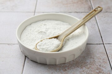Fototapeta na wymiar Baking powder in bowl and spoon on light tiled table, closeup