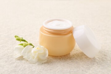 Obraz na płótnie Canvas Body care. Moisturizing cream in open jar and flower on light textured table, closeup