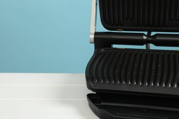 Electric grill on white wooden table against light blue background, space for text. Cooking appliance