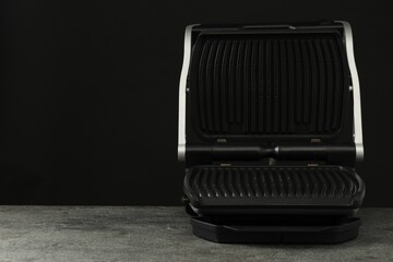 Electric grill on grey textured table against black background, space for text. Cooking appliance