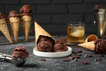 Tasty ice cream scoops, chocolate crumbs and waffle cones on dark textured table, closeup