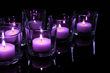 Beautiful burning violet candles on black background, closeup. Funeral attributes