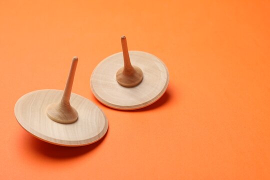 Two wooden spinning tops on orange background, space for text