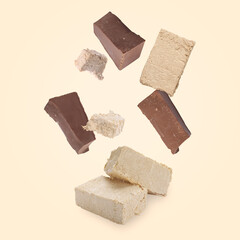 Pieces of tasty halva and chocolate falling on beige background