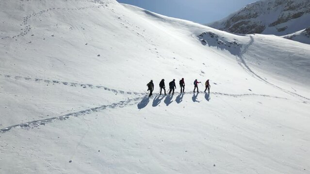 Aerial view of a group of alpinists walking on snow-covered mountain. They wear helmets and safety equipment. Mountaineering, climbing, alpinism concept.