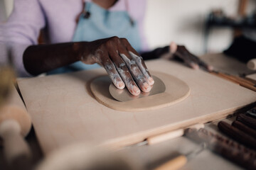 Close up of interracial craftswoman's hand using pottery tool for clay