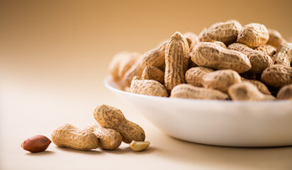 Peanuts. Unshelled nuts in a bowl close up. Roasted pile of peanuts in shell over beige background. Organic vegan, vegetarian food. Healthy nutrition concept.