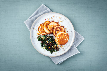 Fototapeta na wymiar Traditional American pancakes with spinach, pine-nuts and raisins served as top view on a Nordic design plate