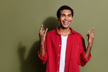 Photo of funky cool guy wear red shirt smiling showing hard rock signs empty space isolated khaki...