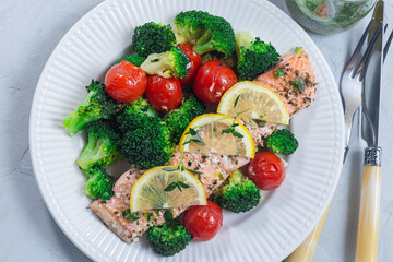 Baked salmon fillet with broccoli and tomato on plate, horizontal, top view