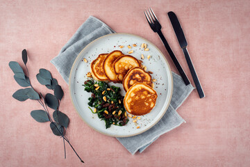 Traditional American pancakes with spinach, pine-nuts and raisins served as top view on a Nordic design plate