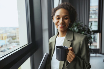 A whitecollar worker gazes out a window with a cup of coffee, smiling - obrazy, fototapety, plakaty